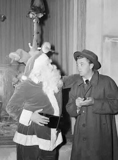 an old black and white photo of two men dressed as santa claus, one holding a bag