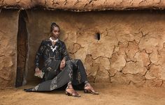 a woman sitting on the ground in front of a mud hut with her legs crossed