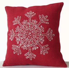 a red pillow with white snowflakes on the front and back, sitting on a table