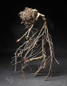 a sculpture made out of branches and twigs on a black background, with the roots still attached to it