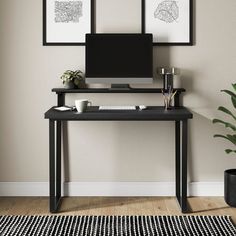 a desk with a computer on it next to a potted plant and two framed pictures