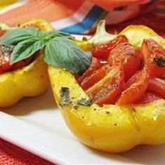 two stuffed peppers with tomatoes and basil on a white platter next to a red table cloth