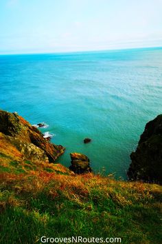 an ocean view from the top of a hill with green grass and rocks on it