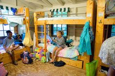 three people sitting on bunk beds in a room with wood flooring and wooden walls