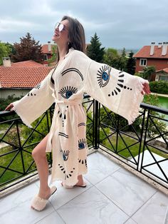 "Beautiful handmade white kimono robe with blue evil eyes, designed with cotton fabric, it flows as you move for a comfortable wear. Beach cover up, a kimono with blue evil eyes.  Beach cover-up, a kimono with an evil eye design.   This is a lovely, good-quality kimono, with traditional breathable kimono sleeves.        A belt that ties around the waist. Great to wear around the house, on beaches, or to dress up with some jeans & a T-shirt, covering up on the beach with a swimsuit.         We love kimonos as they are so versatile. They also make really special & unique birthday, valentines Day, Christmas gifts, and Mother's Day gifts. The perfect combination of comfort and style, this kimono is a great addition to your new season wardrobe.    Cotton Fabric and Handmade      Length from sho Festival Kimono, Belt Kimono, White Kimono, Evil Eye Design, Evil Eyes, Unique Birthday, Kimono Sleeves, Blue Evil Eye, Womens Robes