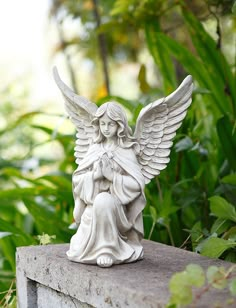 an angel statue sitting on top of a stone wall in the middle of some plants