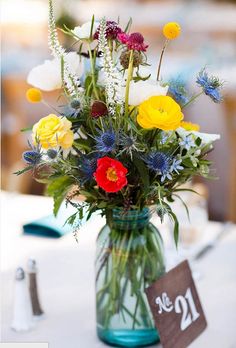 a vase filled with lots of colorful flowers on top of a table next to a sign