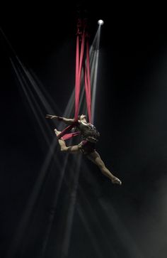 a woman is performing aerial acrobatic tricks on the circus ring with lights behind her