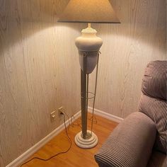 a lamp that is sitting on top of a wooden floor next to a chair and pillow