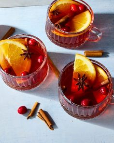 two mugs filled with mulled and orange slices, cinnamon sticks, and cranberries