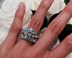 a woman's hand with a diamond ring on it and flowers in the background