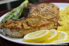 a white plate topped with meat, potatoes and asparagus next to lemon wedges