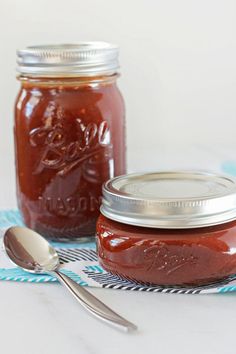 two jars filled with jam sitting on top of a blue and white table cloth next to a spoon