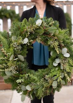 a woman holding a wreath with greenery on it