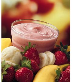 a glass bowl filled with fruit next to bananas and strawberries