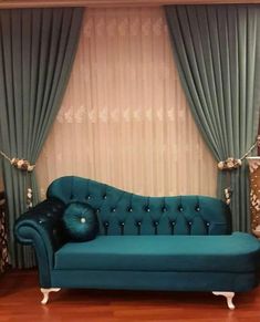 a blue couch sitting in front of a window next to a wall with curtains on it