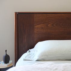 an unmade bed with white linens and wooden headboard, next to a book