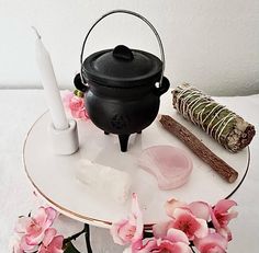 a black pot sitting on top of a white table next to pink flowers and a candle