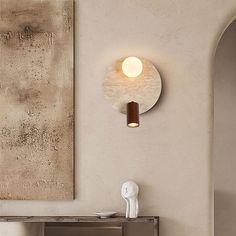 a white vase sitting on top of a wooden table next to a wall mounted light