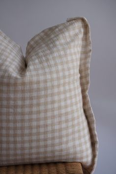 a pillow sitting on top of a wooden chair next to a white and brown checkered pillow