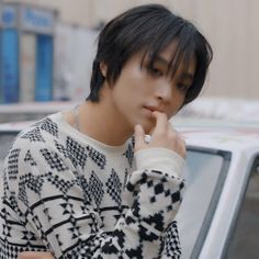 a young man standing in front of a parked car holding his hand to his mouth