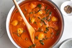 a white bowl filled with tomato soup next to a wooden spoon and some spices on the side