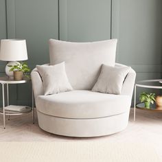 a round chair with pillows on it in front of a green wall and side table