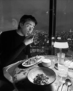 a man sitting at a table with food in front of him and looking out the window