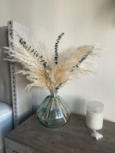 a vase filled with dry grass sitting on top of a wooden table next to a candle