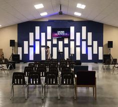 an empty room with rows of chairs in front of a large screen on the wall