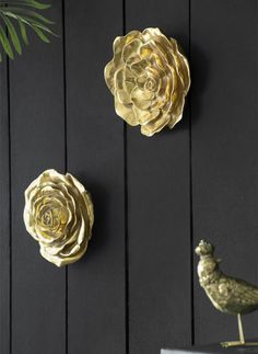 two gold flowers are hanging on a black wall next to a bird and potted plant