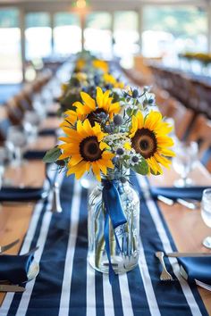 sunflowers are arranged in a mason jar on a striped table runner with blue napkins