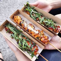 two people holding open boxes with food in them and chopsticks sticking out of the top