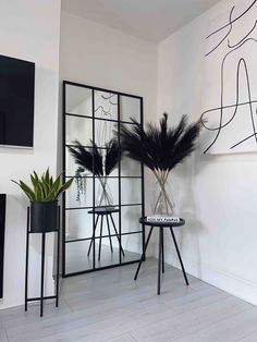 two black vases with plants in them and a mirror on the wall behind them