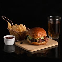 a hamburger and fries on a cutting board with a glass of beer next to it