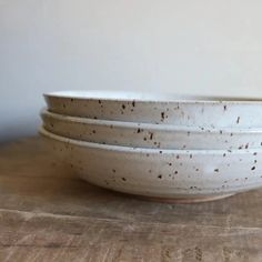 three white bowls with brown speckles on them sitting on a wooden table top