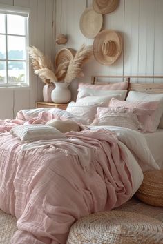 a bed with pink comforter and pillows in a white room next to a window