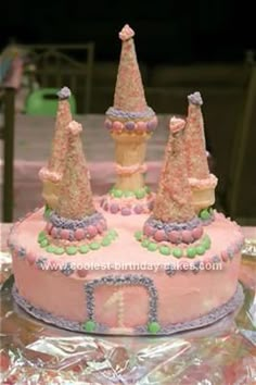 there is a pink cake with castle decorations on the top and sides, sitting on tin foil