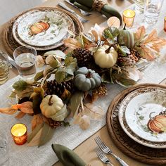 the table is set for thanksgiving dinner with pumpkins, leaves and pineconis