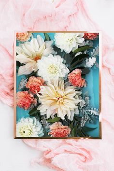 an arrangement of flowers is displayed on a blue and pink background with some feathers around it