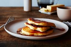 three pancakes on a plate with syrup and butter next to a cup of coffee in the background