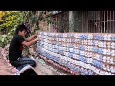 a man sitting on the ground next to a wall covered in bottles and plastic cups