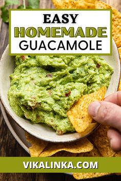 a hand dipping guacamole into a bowl with tortilla chips on the side