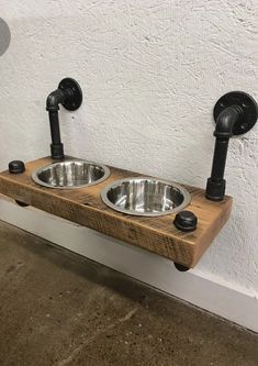 two metal bowls on wooden shelf with black faucets and pipes attached to the wall