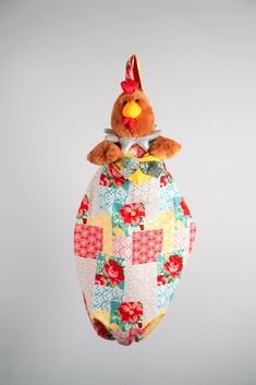 a stuffed chicken hanging from a string on a gray background with red, yellow and blue squares