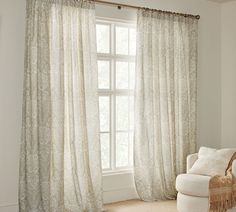 a white chair sitting in front of a window next to a large window with curtains on it