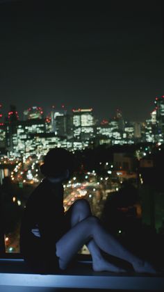 a woman sitting on top of a window sill looking at the city