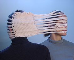 two people with their faces covered by strips of white material, one wearing a black turtle neck sweater