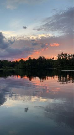 the sky is reflected in the calm lake water at sunset or sunrise, with trees and clouds reflecting on the surface