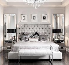 a large white bed sitting in a bedroom next to a chandelier and mirror